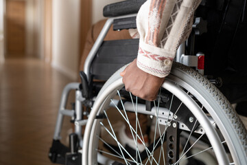 Close-up of man with disability rotating wheels of wheelchair while moving forwards along corridor...