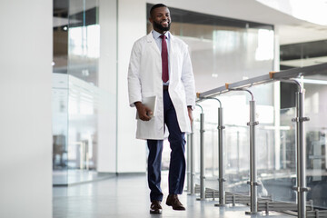 Cheerful black scientist walking by laboratory, holding digital tablet