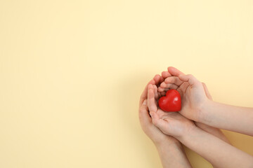 Mother with her child holding red heart on yellow background, top view. Space for text
