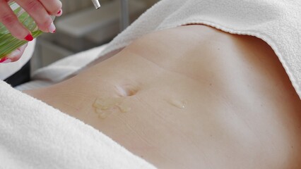 Pouring massage oil on attractive belly of young slim woman. Concept of body care and alternative...