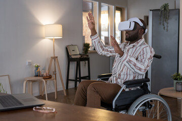 Contemporary software developer in vr headset touching virtual display while sitting in wheelchair and working from home