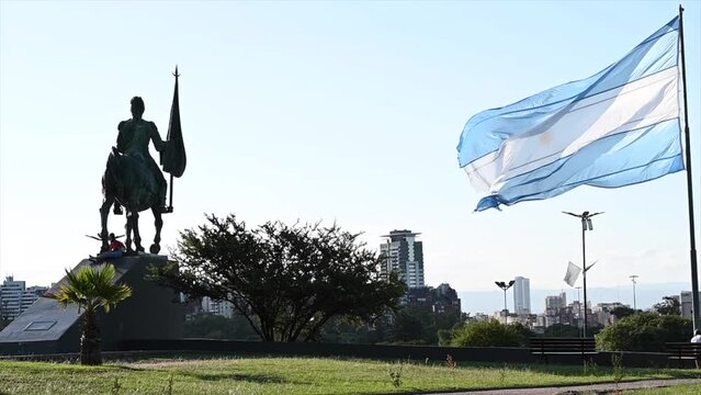 Argentine flag fluttering in slow motion in the wind with statue of Manuel Belgrano
