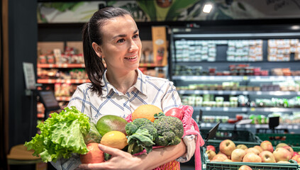 Young woman in a supermarket with vegetables and fruits, buying groceries.