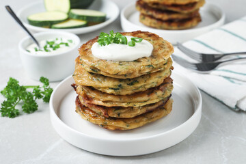 Delicious zucchini pancakes with sour cream served on light grey table