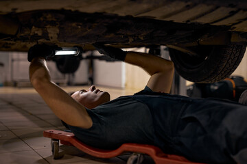Obraz premium concentrated auto mechanic male working alone on floor repairing bottom of car, look at details, troubleshoot the car. young male car mechanic in uniform checking car in automobile service