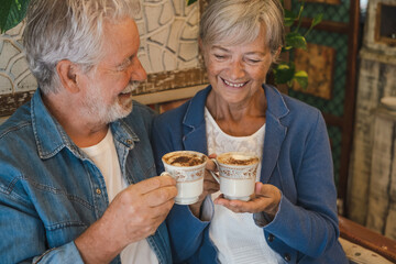 Portrait of a cheerful senior couple inside a coffee shop having break with coffee, cappuccino. Two...