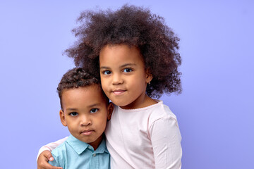 Charming black kids brother and sister twins or siblings in casual wear embracing hugging over purple studio background, copy space. beautiful little cute pretty girl and boy love each other