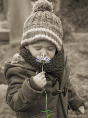 Child smelling flower in spring wearing coat and woollen hat
