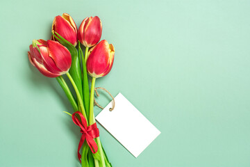 Bouquet of red tulips, white card on green background Top view Flat lay Holiday greeting card Happy moter's day, 8 March, Valentine's day, Easter concept Copy space Mock up