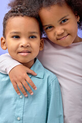 Cute black girl hugging little brother, showing love and affection, purple studio background. Happy...