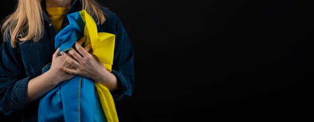 Woman holds ukrainian blue and yellow flag on black background, copyspace blank