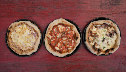 Pizzas. Top view of three pizzas with different ingredients, on the red wooden table. 