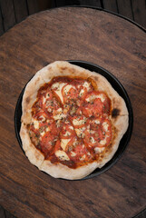 Top view of a traditional Neapolitan pizza with mozzarella cheese, roasted garlic, sliced tomatoes and fresh oregano leaves, on the restaurant wooden table.