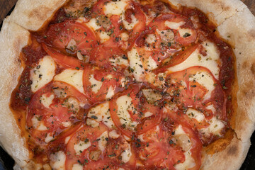 Pizza background. Closeup view of a traditional Neapolitan pizza with mozzarella cheese, roasted garlic, sliced tomatoes and fresh oregano leaves.