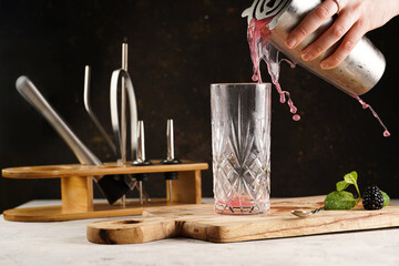 Female bartender hand pouring non-alcoholic mocktail version of the classic blackberry and gin cocktail bramble straining from a cocktail shaker