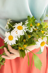 Woman's hands holding bouquet of daisies with orange skirt and blue shirt.