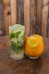 Cocktails. Closeup view of a tropical mojito drink with rum, lime and mint, and a passion fruit daiquiri, on the wooden table.