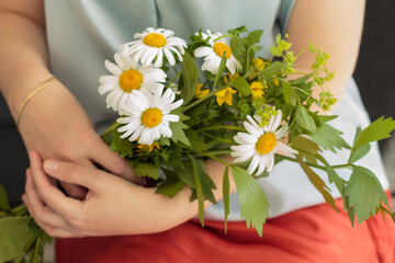 Woman's hands holding bouquet of daisies with orange skirt and blue shirt.