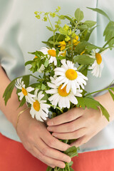 Woman's hands holding bouquet of daisies closeup with orange skirt and blue shirt.