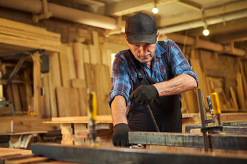 Portrait of a senior carpenter in uniform gluing wooden bars with hand pressures at the carpentry...