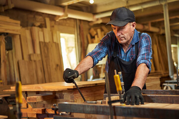 Portrait of a senior carpenter in uniform gluing wooden bars with hand pressures at the carpentry...