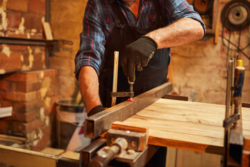 Senior carpenter in uniform gluing wooden bars with hand pressures at the carpentry