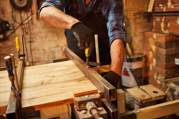 Senior carpenter in uniform gluing wooden bars with hand pressures at the carpentry