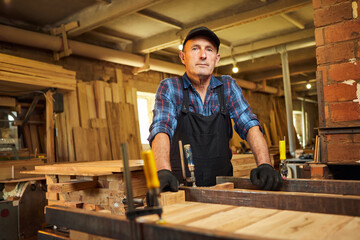 Portrait of a senior carpenter in uniform gluing wooden bars with hand pressures at the carpentry...