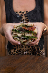 Dining in the restaurant. Closeup view of a woman holding a sliced multilayer vegetarian sandwich...