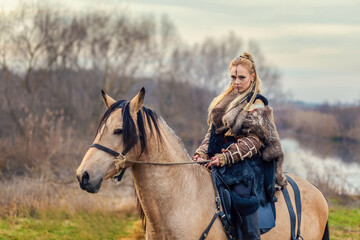 Portrait of beautiful viking woman warrior with painted face and braids riding horse in forest