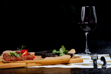 Tartare with black croutons and a glass of red wine on a black background