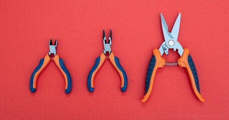 Sheet metal shears orange, blue color rubber handle on red background. Three hand tool various size.