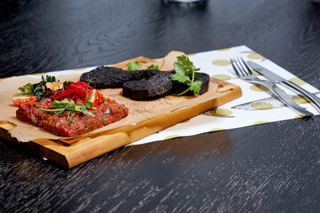 Tartare on a plank beautifully decorated with black croutons and cutlery