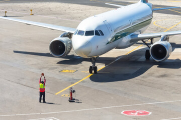 Ground staff airplane marshaller meets passenger plane after landing flight.