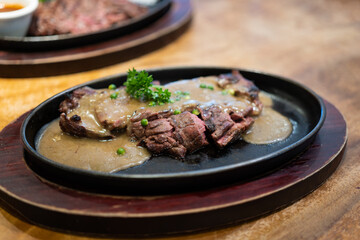 Grilled Juicy steak medium rare beef with herbs and spices on pan hot topped with black pepper sauce on wooden table.