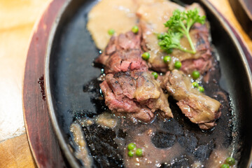 Grilled Juicy steak medium rare beef with herbs and spices on pan hot topped with black pepper sauce on wooden table.