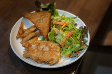 delicious homemade menu, Fried Sea Bass fish fillet in breadcrumbs, buttered bread and fresh vegetable salad served with French Fries on an old wooden table 