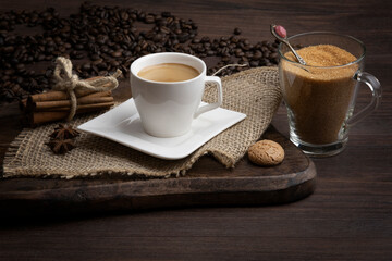 Cup of delicious espresso coffee on dark table with brown sugar, cinnamon, cakes and coffee beans