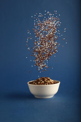 beniseed and linseed pouring into a white bowl against blue background
