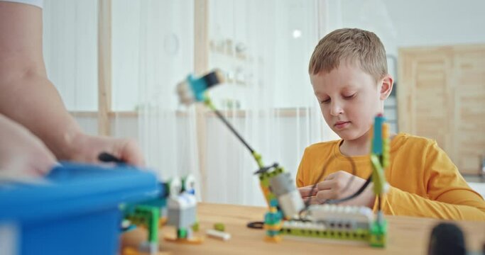 Adorable boy creating electronic construction toy while sitting at table in robotics club
