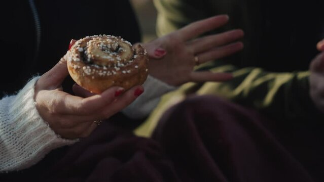 Girl eating delicious cinnamon bun while talking group of friends discussing food baking bakery bake cookie dough buns freshly made pie desert hanging out tea European teen woman hand hands