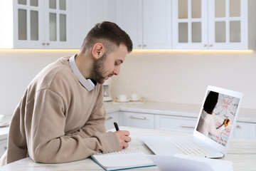 Obraz premium Young man with modern laptop at online lesson in kitchen. E-learning