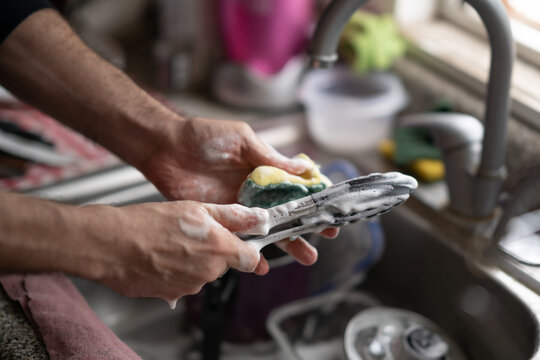 manos masculinas lavando pinzas de metal y trastes con esponja amarilla 