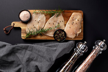 Raw chicken fillet with spices on wooden cutting board, with grey apron and pepper mill. Top view....
