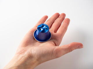 In the men's hand are one blue aluminum coffee capsules. One of the capsules is used. White background. Raw material reuse concept