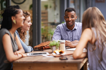 Enjoying good company and a great location. A group of young friends sitting outside at a sidewalk cafe.