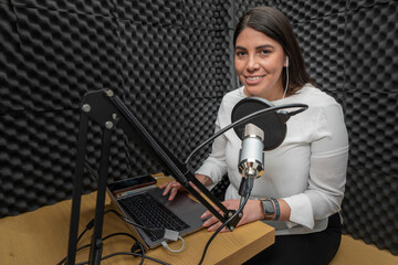 Portrait of a woman smiling while recording a podcast in an audio booth, lined with acoustic...