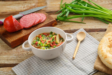Jewish cuisine bean soup cholit on a gray napkin next to green onions, sausage and flatbread.