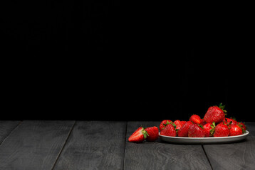 Fresh strawberries on a plate on black wooden table. Dark background. Copy space