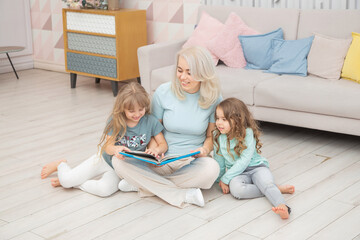 Fototapeta premium Caucasian mom reading a book to children sitting on the floor